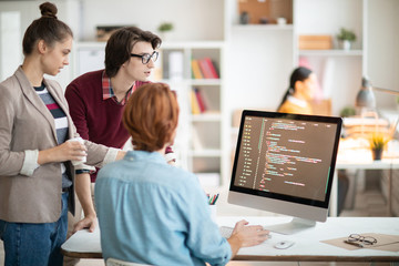 Wall Mural - group of young programmers in casualwear looking at coded data on computer screen and discussing way