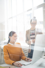 Poster - Two girls in casualwear looking at online data on computer screen while discussing it at meeting in office