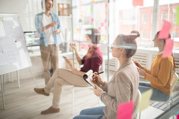 Poster - Group of young casual students with pens and notepads listening to coach and taking part in discussion of new information