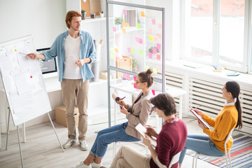 Poster - Young casual coach standing by whiteboard and pointing at one of papers while explaining group of students how to be a success