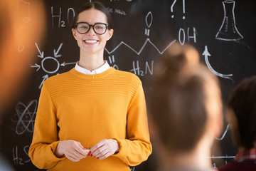 Poster - Young cheerful teacher in casualwear looking at one of students answering her question during discussion of new topic