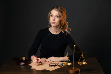 Young lawyer woman in a formal dress sitting at table and writing something by pen, lawyer woman with bright red nails working isolated over the black backgrownd