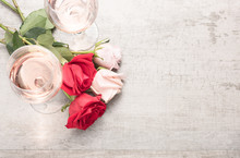 Top Down View Of Two Glasses Of Rosé Wine With Red And Pink Roses On A Reclaimed Wood Background.