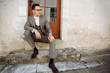 © Kateryna - Perfect style. Handsome young man in a stylish suit and glasses, posing sitting on the stairs on the street and looking away. The groom
