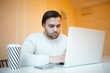 © Lalandrew - Young man using his laptop, wearing white sweater, over yellow.