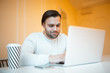 © Lalandrew - Young smiling man using his laptop, wearing white sweater, over yellow.