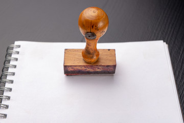 Old wooden rubber stamp on a white piece of notebook. Office accessories on a table.