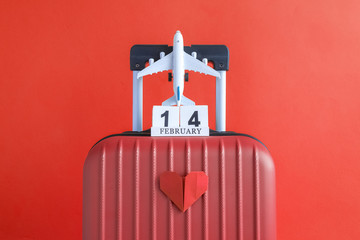 Luggage with valentines day date calendar and aircraft with paper heart on red background minimalistic vacation concept.