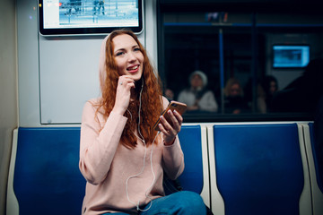 Wall Mural - Positive redhead young female with mobile phone in subway train