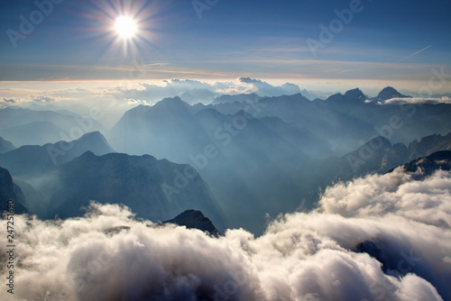 widok-ze-szczytu-triglav-z-niebieskimi-grzbietami-pasma-julijske-alpe-w-sloncu-bialymi-chmurami-o-niskim-haldzie-zamglona-dolina-trenta-soca-isonzo-i-szczytem-bavski-grintavec-park-narodowy-triglav-slowenia-europa
