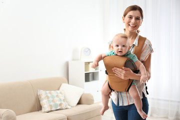 Sticker - Woman with her son in baby carrier at home. Space for text