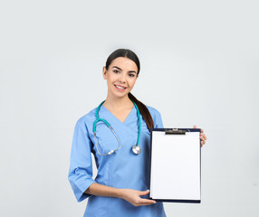 Wall Mural - Portrait of medical assistant with stethoscope and clipboard on light background. Space for text