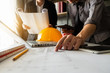 © Nuttapong punna - Two colleagues discussing data working and tablet, laptop with on on architectural project at construction site at desk in office