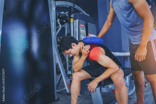 Cuadros en Lienzo Fit man with shoulder suffering pain has treated with hot compress by his buddy after workout at fitness gym
