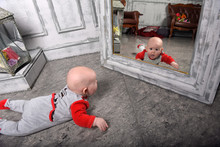 Newborn Baby In Red With Gray Clothes In Front Of The Mirror Looks At Himself
