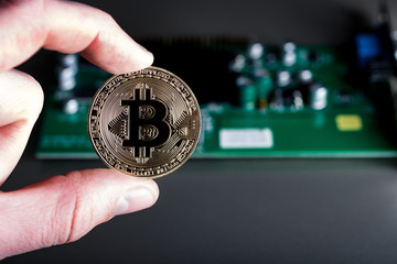 man holding bitcoin coins with two fingers on the background of electric circuit Board