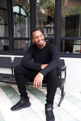 Handsome cheerful african american man in black polo sitting on bench