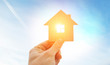 © SkyLine - Man's hand holds wooden flat house against the sun
