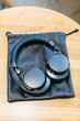 Photo of black wireless headphones with leather storage bag on wooden textured table/ music time, flat lay, selective focus on headset, top view with copy space/ music and lifestyle concept.