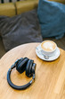 Picture of black wireless headphones and white cup of coffee on wooden table/ enjoying coffee in a cafe, music time, selective focus on headset, top view with copy space/ music and lifestyle concept.