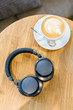 Shot of black wireless headphones and white cup of coffee on wooden table/ listening music with headphone, music time, flat lay, headset, top view with copy space/ music and lifestyle concept.