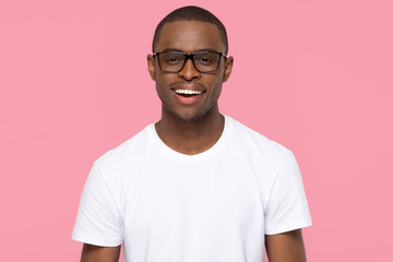 Portrait of happy confident handsome african american black man with attractive face and white dental smile wearing optical glasses t-shirt looking at camera isolated on blank pink studio background.