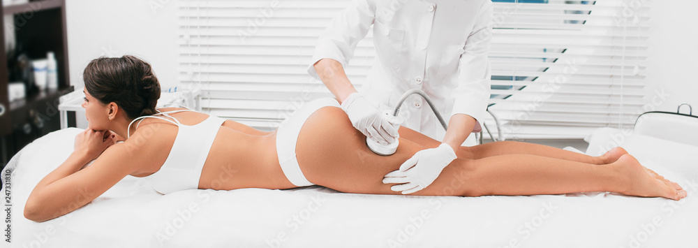 Beautiful woman having cavitation, procedure removing cellulite on legs and buttocks at beauty clinic - obrazy, fototapety, plakaty 
