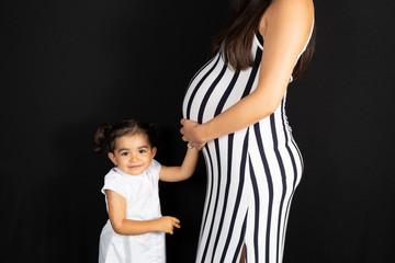 cute pretty child daughter touching belly mother pregnant in black and white dress