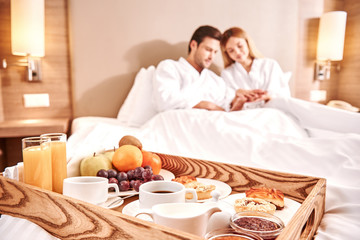 Food in a bed. Couple are hugging in hotel room bed