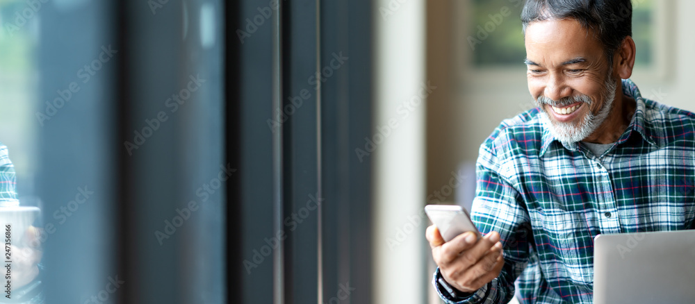Banner of happy mature asian or hispanic old man looking at smartphone smiling positive in casual lifestyle with digital technology of older or senior guy concept. Urban elderly asian retired man. - obrazy, fototapety, plakaty 