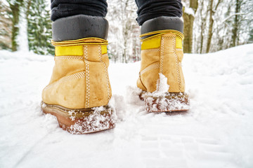 Wall Mural - Winter Walk in Yellow Leather Boots. Back view on the feet of a man walking along the icy snowy pavement. Pair of shoe on icy road in winter. Abstract empty blank winter weather background