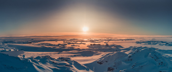 Wall Mural - bright sunset panorama view in antarctica. orange sun lights over the snow covered polar surface. pi