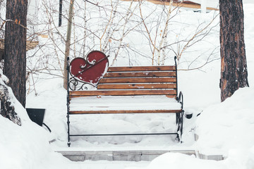 Snow-covered bench in the park with a heart shaped decoration