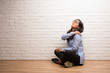 © Asier - Young indian woman sit against a brick wall with back pain due to work stress, tired and astute