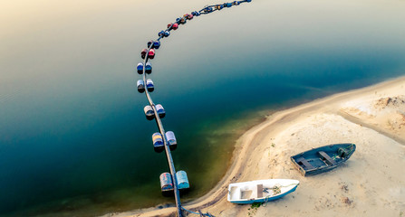 Aerial view of blue tube with barrels on the lake and two boates on sandy beach