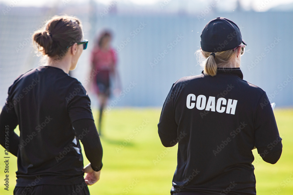 Back view of female sport coach and her assistant in black COACH shirt at an outdoor sport field - obrazy, fototapety, plakaty 
