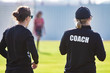 Back view of female sport coach and her assistant in black COACH shirt at an outdoor sport field