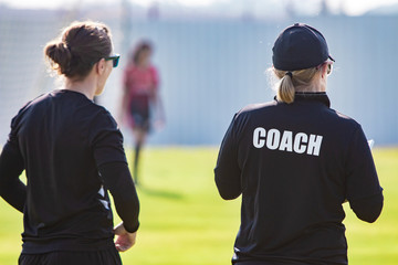 back view of female sport coach and her assistant in black coach shirt at an outdoor sport field