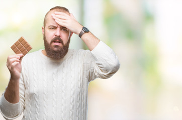 Sticker - Young hipster man eating chocolate bar over isolated background stressed with hand on head, shocked with shame and surprise face, angry and frustrated. Fear and upset for mistake.