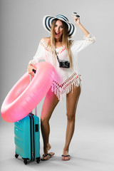 Wall Mural - Full body young pretty woman ready for vacation holding a pink float and her baggage