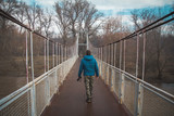 Fototapeta  - Young man crossing a bridge in the forest