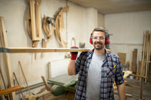 Portrait Of Young Woodworker Holding Wood In His Carpentry Workshop.