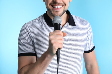 Handsome man in casual clothes holding microphone on color background, closeup