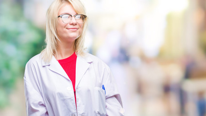 Poster - Young beautiful blonde professional woman wearing white coat over isolated background looking away to side with smile on face, natural expression. Laughing confident.