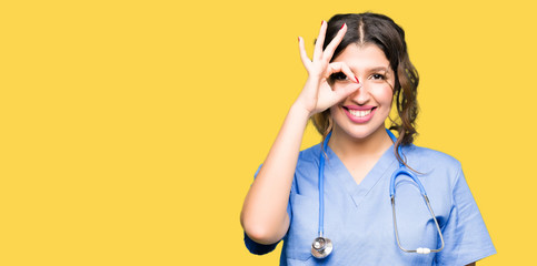 Young adult doctor woman wearing medical uniform doing ok gesture with hand smiling, eye looking through fingers with happy face.