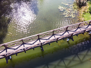 old wooden footbridge over river. sky and sun reflecting in greenish water. aerial top image  