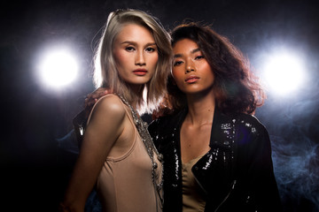 Wall Mural - Two Fashion Young thin Asian Woman Tan skin eyes beautiful make up fashion dress lesbian look posing attractive glam look. Studio Lighting Dark Background smoke fog back rim light low exposure