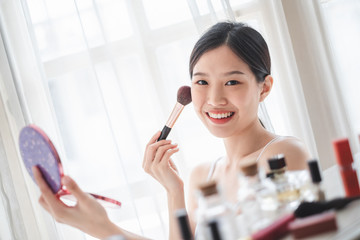 Wall Mural - Young beautiful Asian woman applying cosmetics make up on her face, health beauty skin care and make up concept