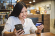 © Nattakorn - Young beautiful asian woman using smart phone and credit card for shopping online in coffee shop cafe