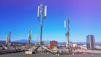 Cellular network antenna radiating and broadcasting strong power signal waves over the city on a building roof with telecommunication mast